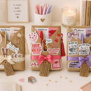 May include: Three wrapped book gifts with decorative stickers, bows, and tags. The gifts are brown paper with pink, purple, and cream ribbons. The gifts have stickers that say "Hot Read Books", "One More Page", and "Bookish".