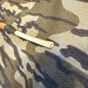 Puede incluir: Una pipa de fumar de madera con una boquilla de color claro y un v&aacute;stago de color oscuro. La pipa descansa sobre un fondo de tela de camuflaje. La pipa es de dise&ntilde;o tradicional, con forma cil&iacute;ndrica.