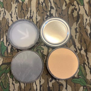 May include: Four round, lidded containers with different coloured interiors. The lids are black with a silver rim. The interiors are white, grey, brown, and silver.