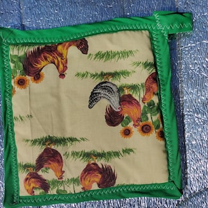 May include: Green pot holder with a white background and a rooster pattern. The pot holder has a loop for hanging.