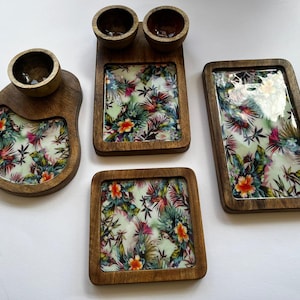 Könnte beinhalten: Vier Serviertabletts aus Holz mit tropischen Blumenmustern. Die Tabletts sind in verschiedenen Größen und Formen erhältlich, einige mit kleinen Schalen.