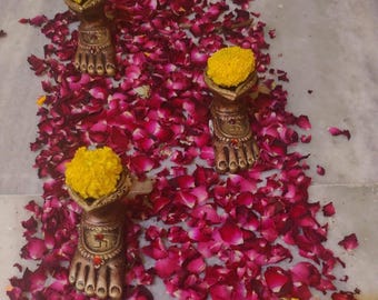 May include: Three decorative golden foot-shaped holders with yellow flowers on top, surrounded by red rose petals.