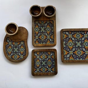 Könnte beinhalten: Vier Holztabletts mit aufwendigen blauen, grünen und orangefarbenen Mustern. Die Tabletts eignen sich perfekt zum Servieren von Snacks, Vorspeisen oder Desserts.