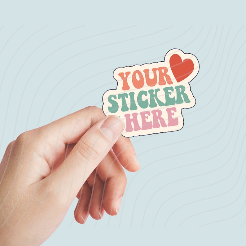 May include: A sticker with the text "YOUR STICKER HERE" in a retro font with a red heart. The sticker is being held by a hand.