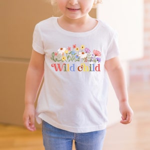 Peut inclure: T-shirt blanc avec un motif floral color&eacute; et le texte "Wild child" en couleurs arc-en-ciel.