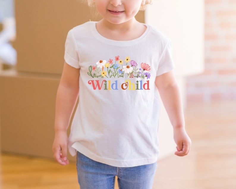 Peut inclure: T-shirt blanc avec un motif floral color&eacute; et le texte "Wild child" en couleurs arc-en-ciel.