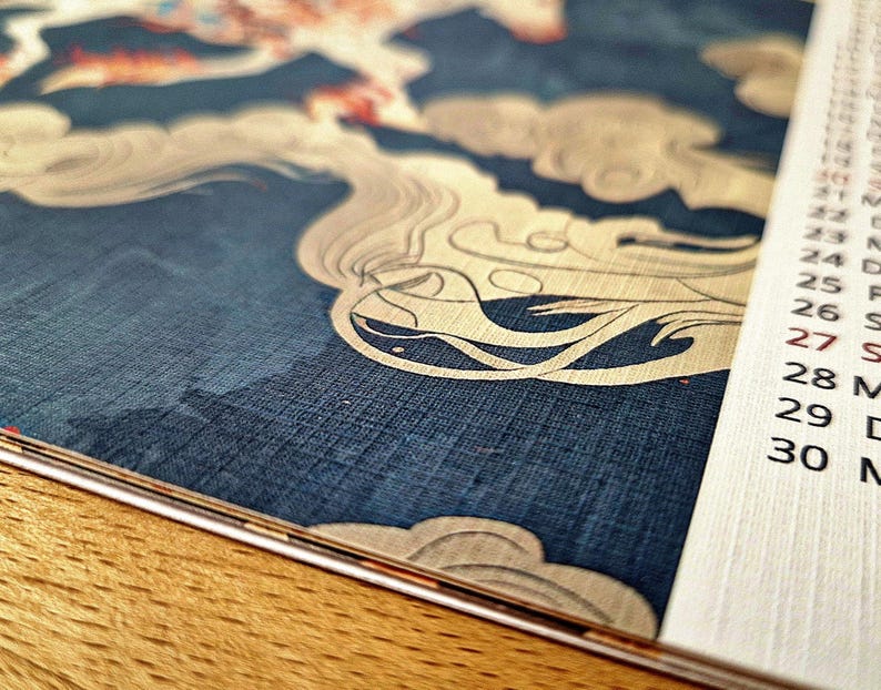 May include: Close-up of a calendar with a decorative blue and cream design. The design features a stylized cloud pattern. The calendar pages are white with black text, showing the days of the month.