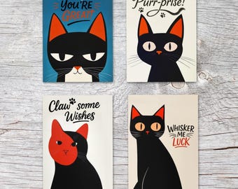 Op de afbeelding: Vier wenskaarten met illustraties van cartoonkatten. Elke kaart toont een zwarte kat met oranje oren en ogen, en een andere woordspeling: "Fur Real, You're Great", "Purr-prise!", "Claw some Wishes" en "Whisker Me Luck".