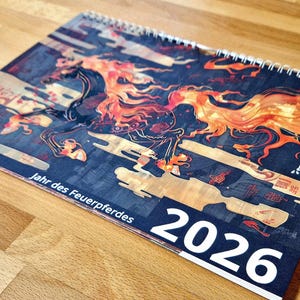 May include: A spiral-bound calendar for 2026 featuring a stylized illustration of a fiery horse in shades of orange, red, and black against a dark blue background. The calendar has text in German and Japanese.