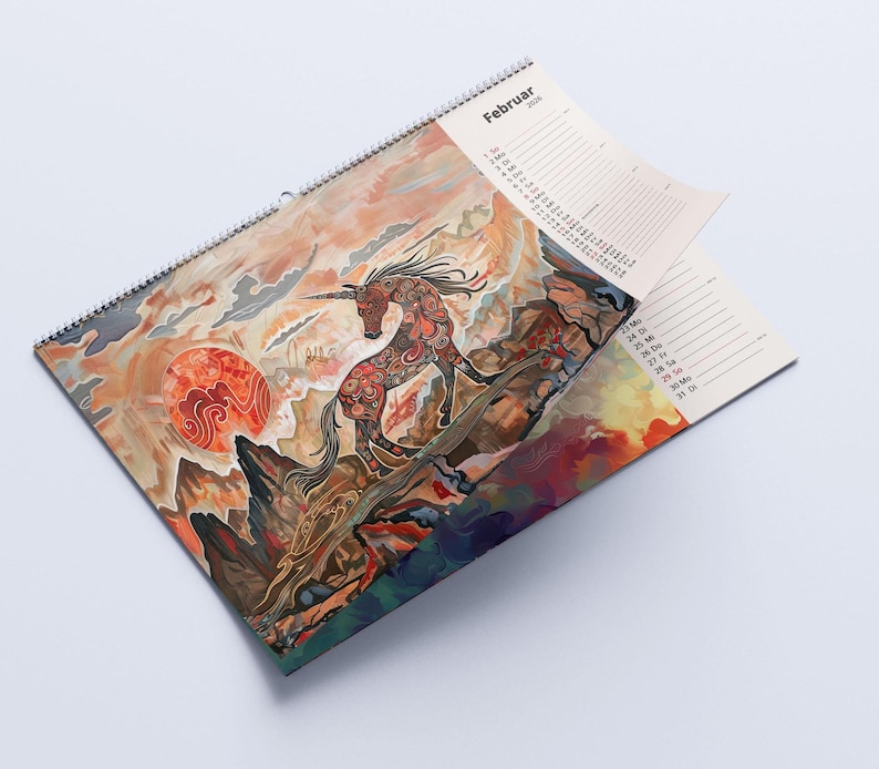 May include: A spiral-bound calendar featuring a vibrant illustration of a unicorn against a sunset backdrop. The artwork includes a red sun and detailed mountain scenery. The word "Februar" is visible at the top.