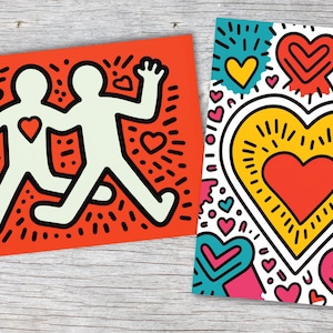 Puede incluir: Dos impresiones art&iacute;sticas de estilo pop art. Una es naranja con dos figuras tomadas de la mano, cada una con un coraz&oacute;n. La otra es blanca con un gran coraz&oacute;n amarillo y corazones m&aacute;s peque&ntilde;os en rosa, azul y amarillo.