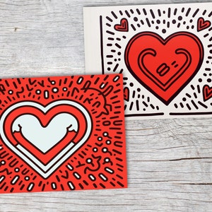 Puede incluir: Dos impresiones art&iacute;sticas con dise&ntilde;os de coraz&oacute;n. Una impresi&oacute;n tiene un fondo rojo con un coraz&oacute;n blanco y contornos negros. La otra impresi&oacute;n tiene un fondo blanco con un coraz&oacute;n rojo y contornos negros. Ambas impresiones son de estilo pop art.