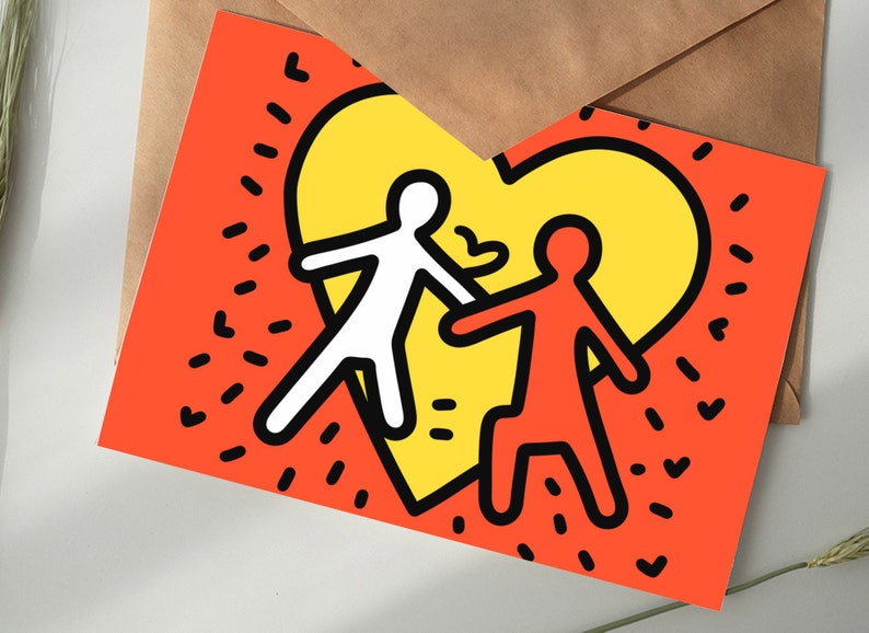 Puede incluir: Tarjeta de felicitaci&oacute;n con una ilustraci&oacute;n estilizada de dos figuras abraz&aacute;ndose dentro de un coraz&oacute;n amarillo sobre un fondo naranja. Las figuras est&aacute;n delineadas en negro, una blanca y otra naranja. La tarjeta est&aacute; sobre una superficie blanca.