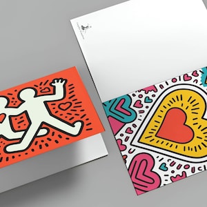 Puede incluir: Dos tarjetas de felicitaci&oacute;n con dise&ntilde;os coloridos. Una tarjeta presenta dos figuras blancas con un coraz&oacute;n sobre un fondo naranja. La otra tarjeta tiene un gran coraz&oacute;n con contorno amarillo y centro rojo, rodeado de corazones y acentos coloridos.