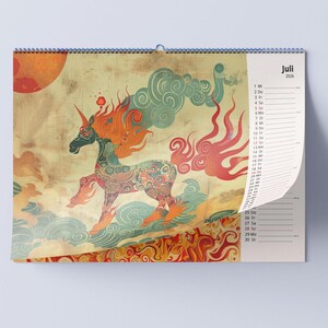 May include: A wall calendar featuring a colorful illustration of a unicorn with flowing orange and red mane and tail. The unicorn is set against a backdrop of clouds and a large orange sun. The calendar is dated July 2025.