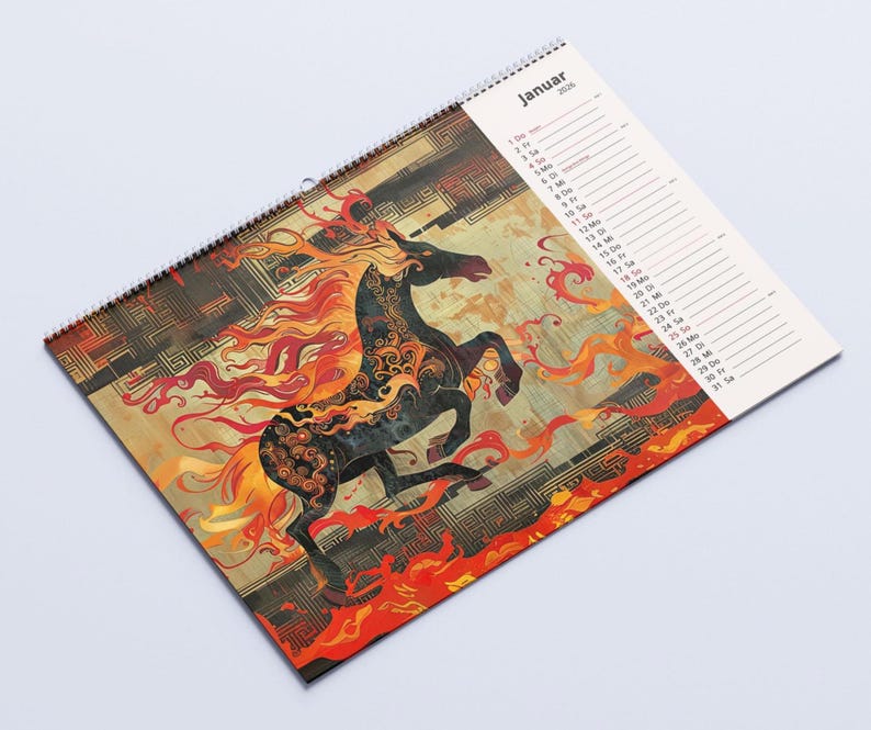 May include: A spiral-bound calendar featuring a stylized black horse with fiery red and orange mane and tail. The horse is set against a background of gold and brown geometric patterns. The calendar is labeled "Januar 2026".