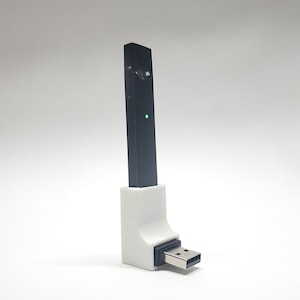 Może przedstawiać: Biała ładowarka ze złączem USB do czarnego e-papierosa.