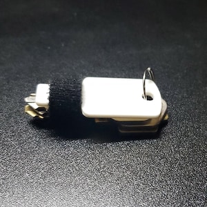 May include: A white key fob with a black fabric strap and a silver ring. The fob has a small white rectangular tag with a hole in the top.