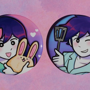 May include: Two round button badges featuring cartoon characters. The first badge depicts a girl with purple hair and a pink bow holding a yellow bunny. The second badge shows a boy with purple hair and a blue shirt holding a spatula.
