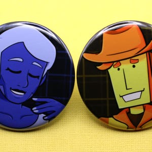 K&ouml;nnte beinhalten: Zwei runde Ansteckbuttons mit illustrierten Charakteren. Der linke Button zeigt eine blauh&auml;utige Figur mit hellem Haar und geschlossenen Augen. Der rechte Button zeigt eine gelbh&auml;utige Figur, die einen orangefarbenen Hut und ein Hemd tr&auml;gt.