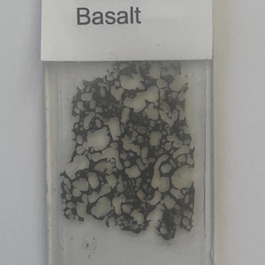 Handgjord geologisk tunn sektion framställd på begäran - Vesikulär porfyrisk olivinbasalt (ibland kallad oceanit) från Hawaii, USA.