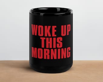 May include: Black coffee mug with the words "WOKE UP THIS MORNING" in red block letters. The mug is sitting on a wooden surface.