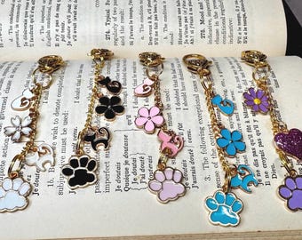 May include: A gold chain with various charms, including paw prints, flowers, and hearts. The charms are in different colors, including white, black, pink, blue, purple, and glitter. The charms are attached to a gold chain with a lobster clasp.