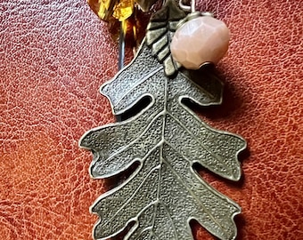 May include: A brown leather bag with a metal charm featuring an oak leaf, an acorn, and a pink stone.