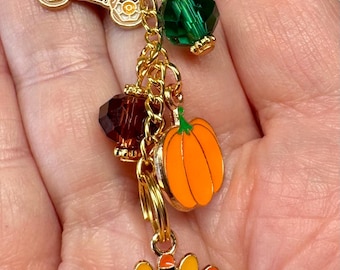 May include: A gold-toned charm bracelet with Thanksgiving-themed pendants. Charms include a wagon filled with produce, a green faceted bead, a brown faceted bead, an orange pumpkin, and a turkey wearing a hat.