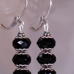 May include: A pair of silver dangle earrings with three black faceted beads on each earring.