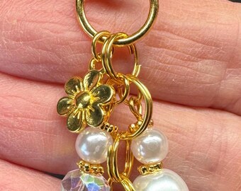 May include: Gold-coloured keychain with a lobster clasp, flower charm, faux pearls, and a crystal bead. A small, orange and white fox charm hangs at the bottom. The keychain is designed for keys or accessories.