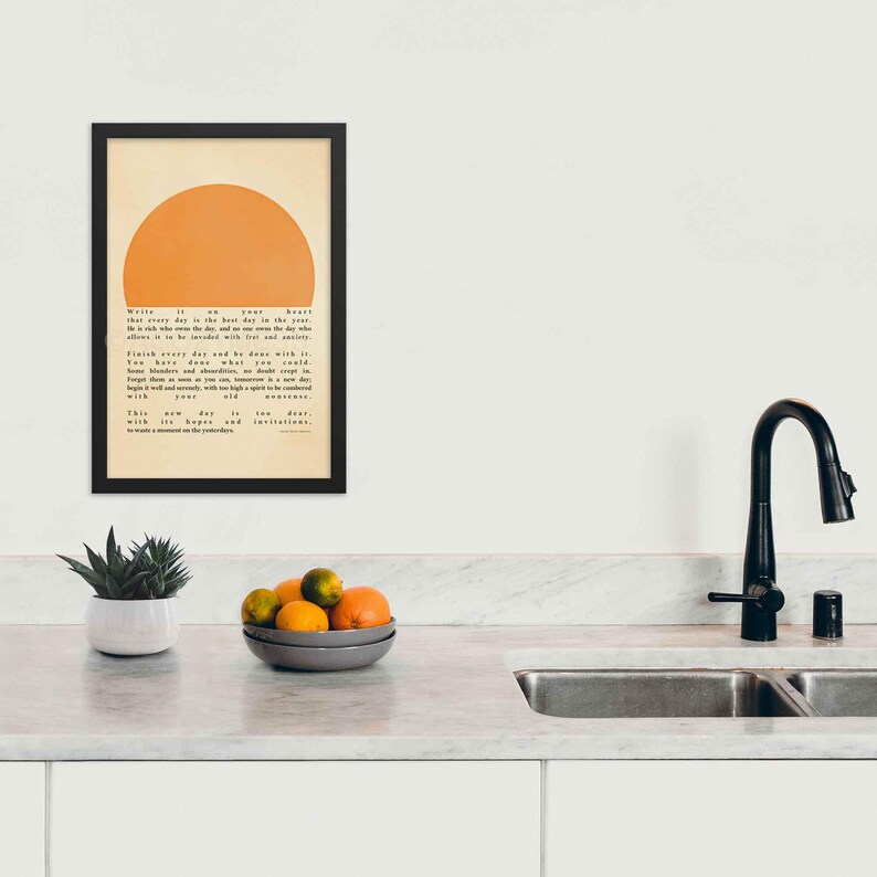 Ralph Waldo Emerson's Poster featuring  inspirational quote, Write it on your heart..., with a warm sun illustration, displayed in a black frame, on a kitchen wall.
