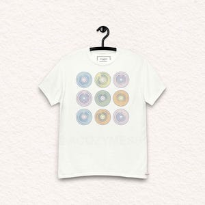 Puede incluir: Camiseta blanca con un diseño gráfico de nueve discos de vinilo de color pastel.