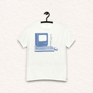 Könnte beinhalten: Ein weißes T-Shirt mit einer blauen Umrandung eines Vintage-Computers, einer Tastatur und einer Maus. Eine einzelne Blume steht in einer Vase neben dem Computer.