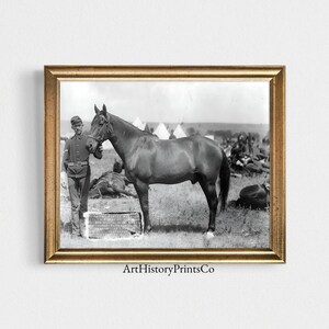 May include: A black and white photograph of a soldier standing next to a horse in a military camp. The soldier is wearing a uniform and a hat. The horse is standing on a grassy field. There are tents in the background.