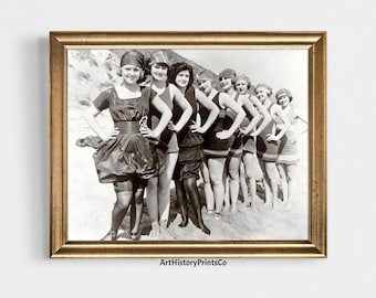 May include: A framed black and white photograph featuring a group of women in vintage swimwear posing on a beach. The women are wearing swimsuits, hats, and bloomers. The photograph is in a gold-colored frame. The text "ArtHistoryPrintsCo" is visible.