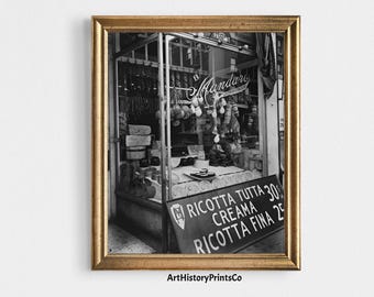 Può includere: Stampa in bianco e nero incorniciata di un negozio di gastronomia italiano vintage. La vetrina mostra salumi appesi, formaggi e un'insegna con testo italiano. La cornice è dorata.