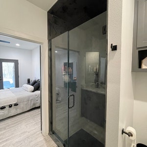 May include: A modern bathroom featuring a black glass shower door and a black shower floor. The shower has a black handle and a black shower head. The bathroom has white walls and a white toilet.