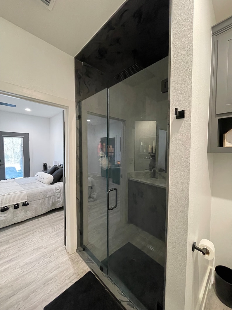 May include: A modern bathroom featuring a black glass shower door and a black shower floor. The shower has a black handle and a black shower head. The bathroom has white walls and a white toilet.
