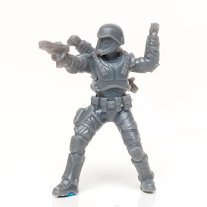Könnte beinhalten: Ein grauer Plastik-Spielzeugsoldat in Kampfhaltung, der eine Pistole in der rechten Hand hält und die linke Hand hebt. Die Figur trägt einen Helm, eine Körperpanzerung und taktische Ausrüstung. Das Spielzeug steht vor weißem Hintergrund.