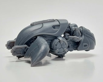 May include: A gray plastic model of a futuristic vehicle with intricate details and a sleek design. The vehicle has a rounded body with a large, open cockpit and a series of small, detailed wings.