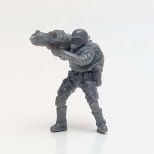 May include: A gray plastic miniature figure of a soldier holding a futuristic weapon. The soldier is wearing a helmet and has a backpack.