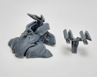 Puede incluir: Un modelo de nave espacial de plástico gris con un sistema de armas desmontable. La nave espacial tiene una cabina y un gran motor en la parte trasera. El sistema de armas es un conjunto de cuatro cañones montados en una base.