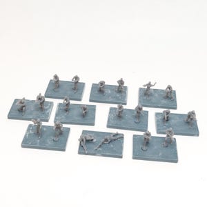 Pode incluir: Uma coleção de miniaturas de soldados de plástico cinza em bases retangulares. As figuras estão em várias poses, incluindo em pé, correndo e deitadas. As bases são de uma cor cinza-azulada suave.