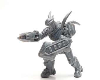 May include: A gray plastic action figure of a robot with a shield and a gun. The robot has a pointed head and a detailed design.