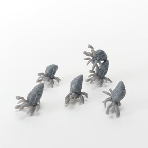 Puede incluir: Cinco criaturas grises en miniatura con tentáculos están dispuestas sobre una superficie blanca. Cada criatura tiene un cuerpo cónico y múltiples apéndices. Las criaturas parecen pequeñas figuras o modelos.