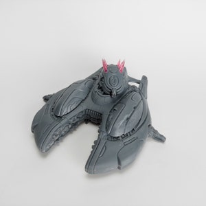 May include: A grey, detailed, spaceship model with pink accents. The spaceship has a rounded, open cockpit and two wings that are folded down.