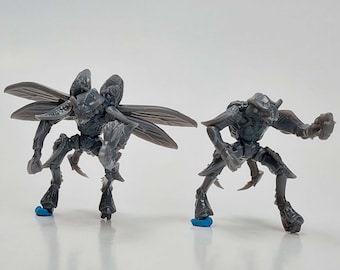 Pode incluir: Duas figuras cinzentas com forma de inseto, com exoesqueletos detalhados e membros articulados. Uma tem asas grandes, a outra posa com um braço levantado. Ambas estão sobre pequenas bases azuis, num fundo branco.