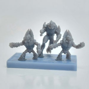 Pode incluir: Três figuras de plástico cinzento de guerreiros alienígenas. As figuras estão em pé sobre uma base azul. As figuras são detalhadas e têm armas.