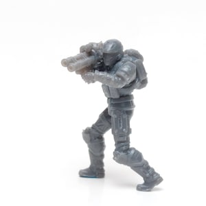 May include: A gray plastic action figure of a soldier holding a large gun. The figure is wearing a helmet and armor.